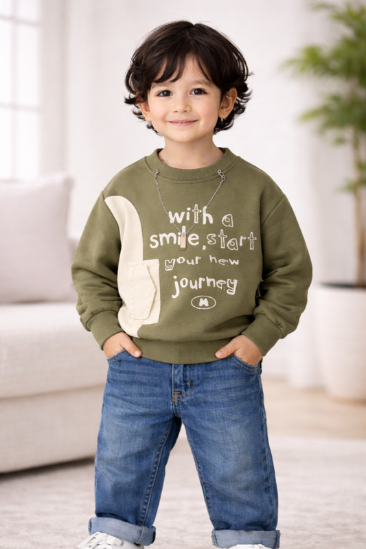 Child wearing a green sweatshirt with text and jeans indoors